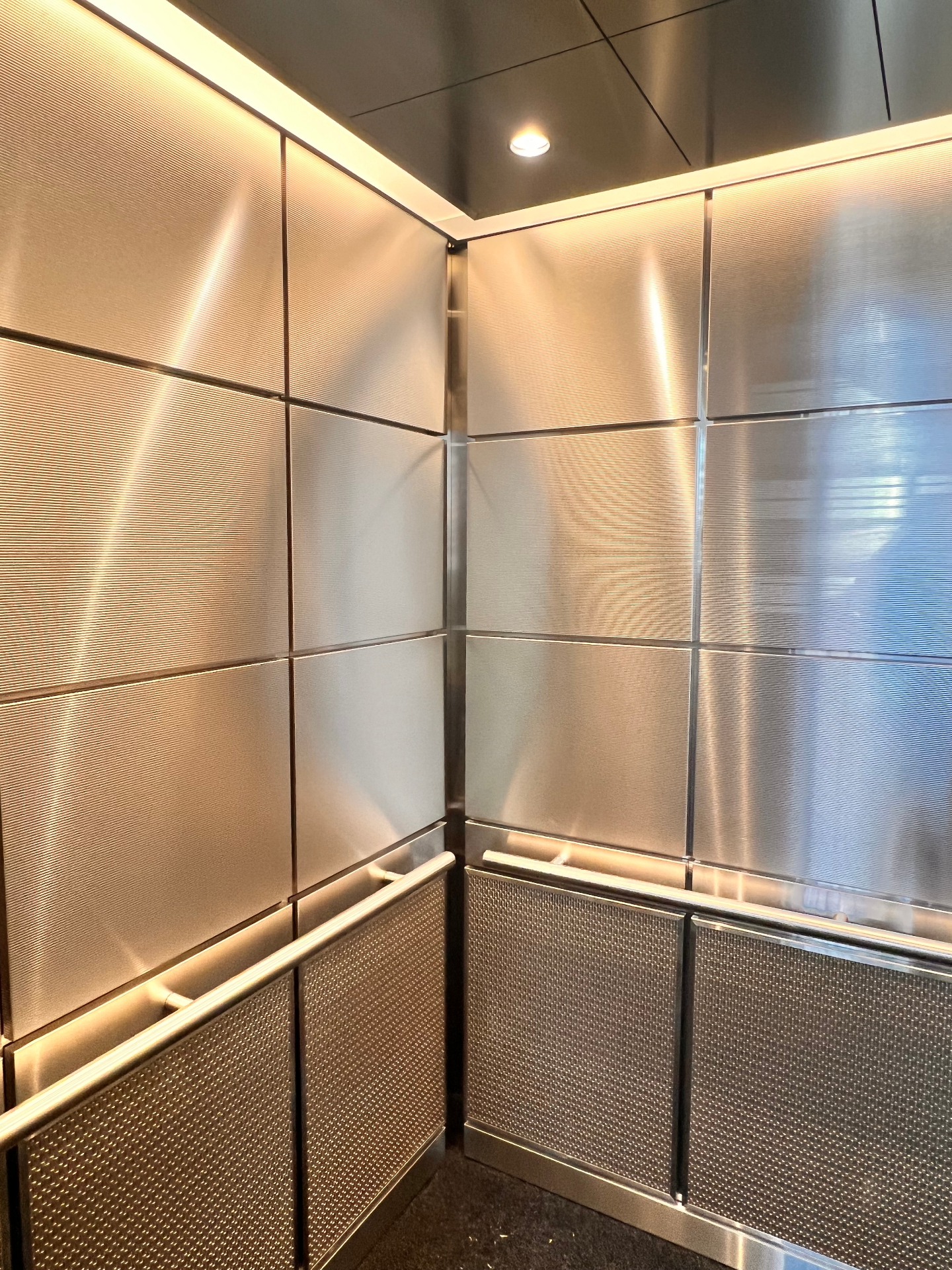 Elevator interior with patterned metal wall panels, stainless rails, and recessed ceiling lights