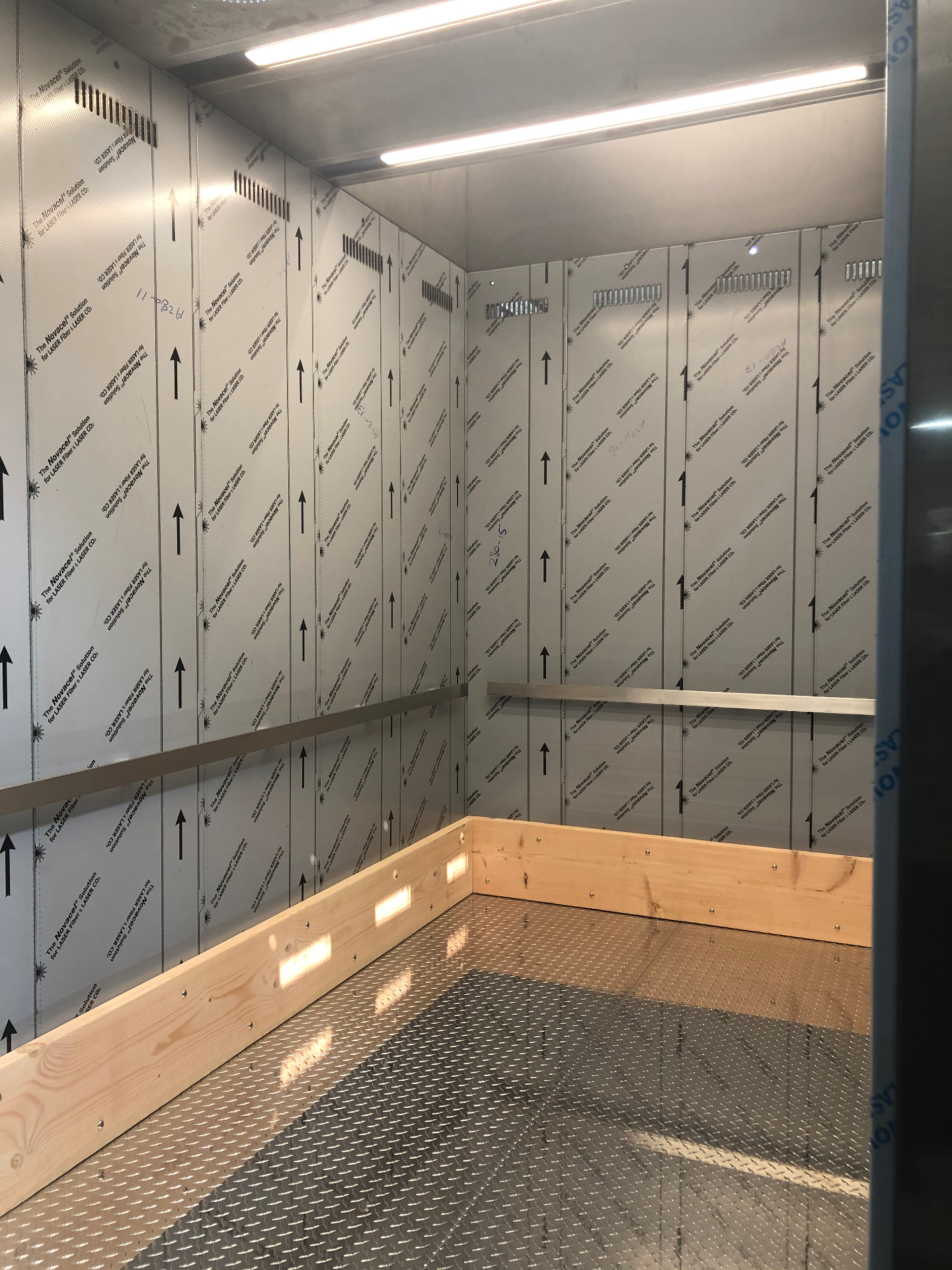 Freight elevator cab during fit-out with protective panels, wood bumper guards, and metal flooring