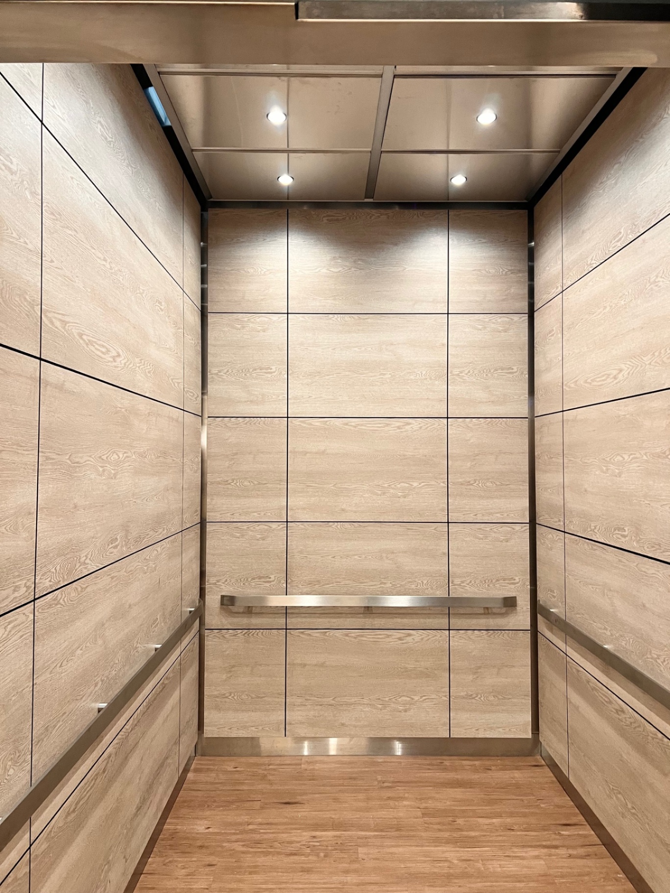 Elevator interior with light oak-style panels, integrated downlights, and stainless rails