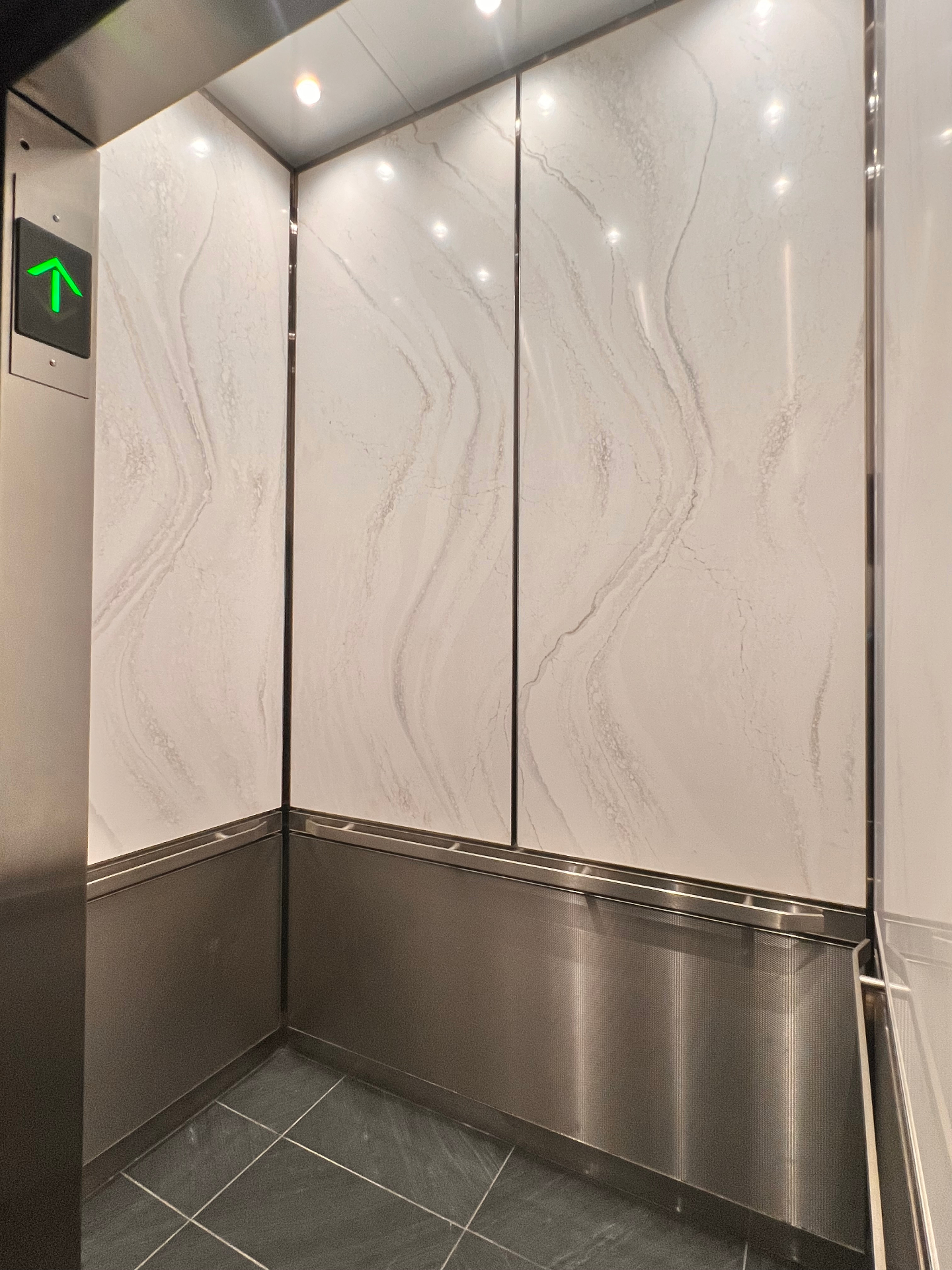 Elevator interior with stone-look wall panels, stainless lower panels, and handrail detailing