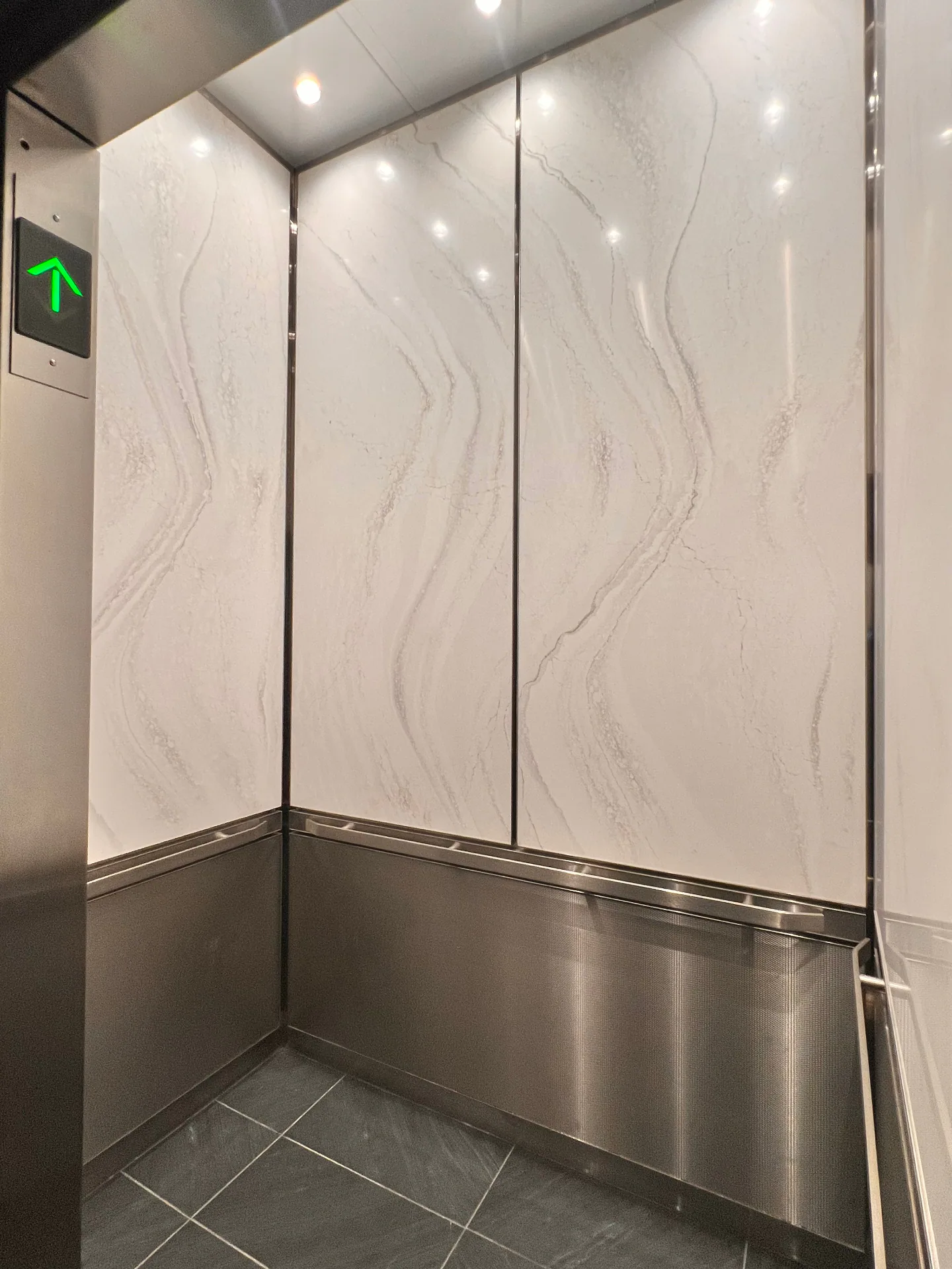 Elevator interior with stone-look wall panels, stainless lower panels, and handrail detailing