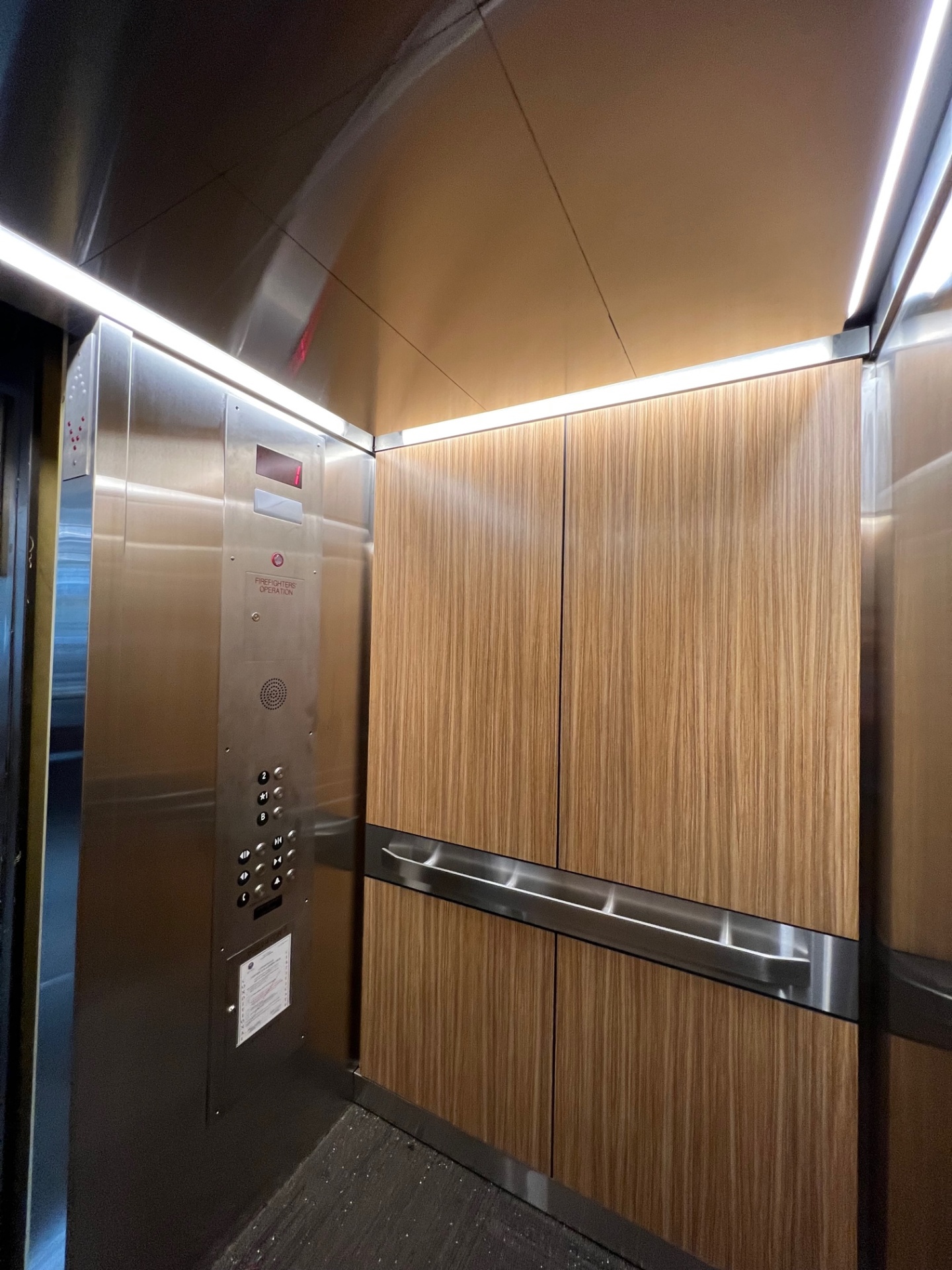 Custom elevator interior with warm wood veneer panels, stainless trim, and integrated lighting