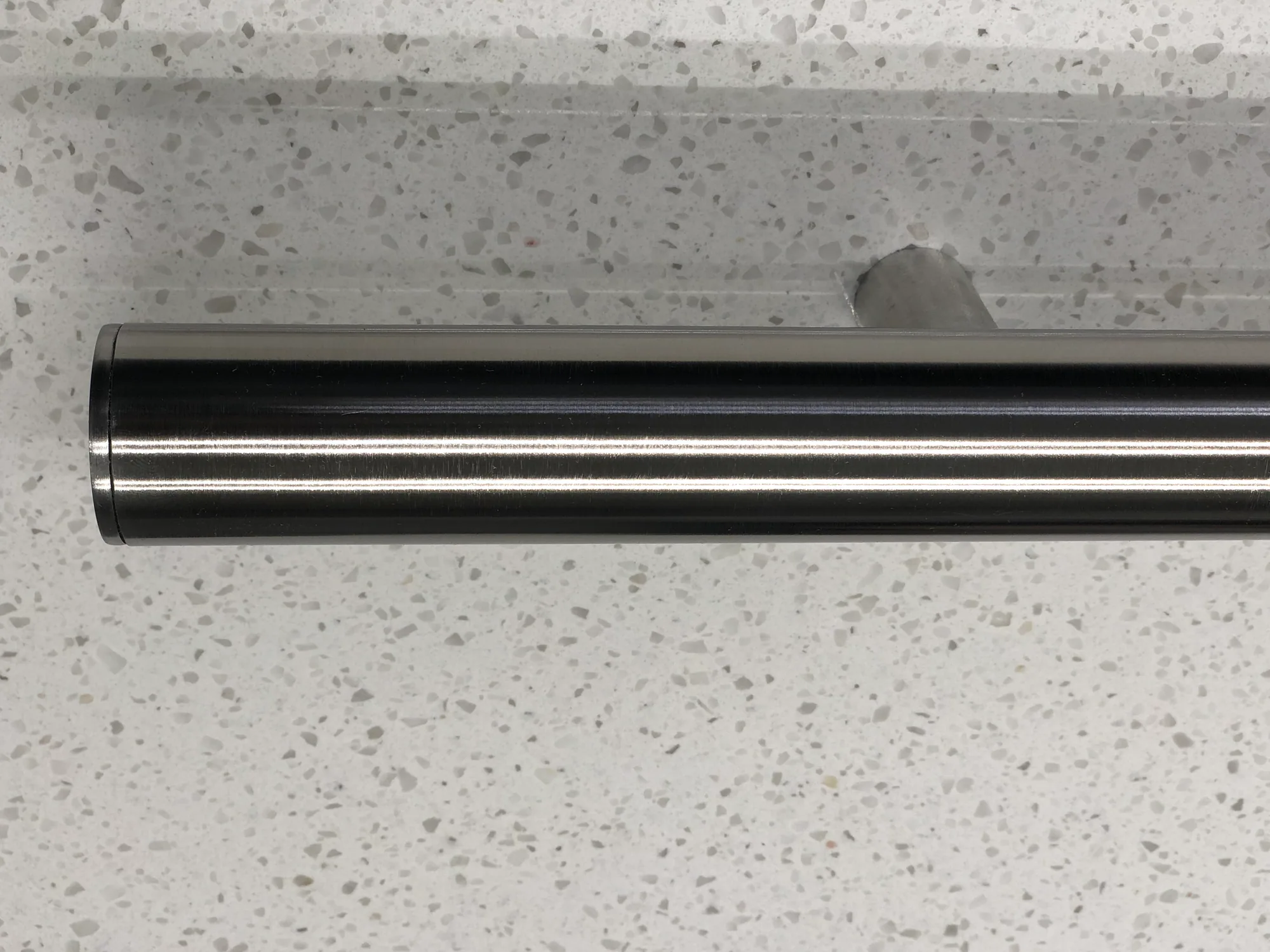 Round stainless steel elevator handrail mounted against a stone surface