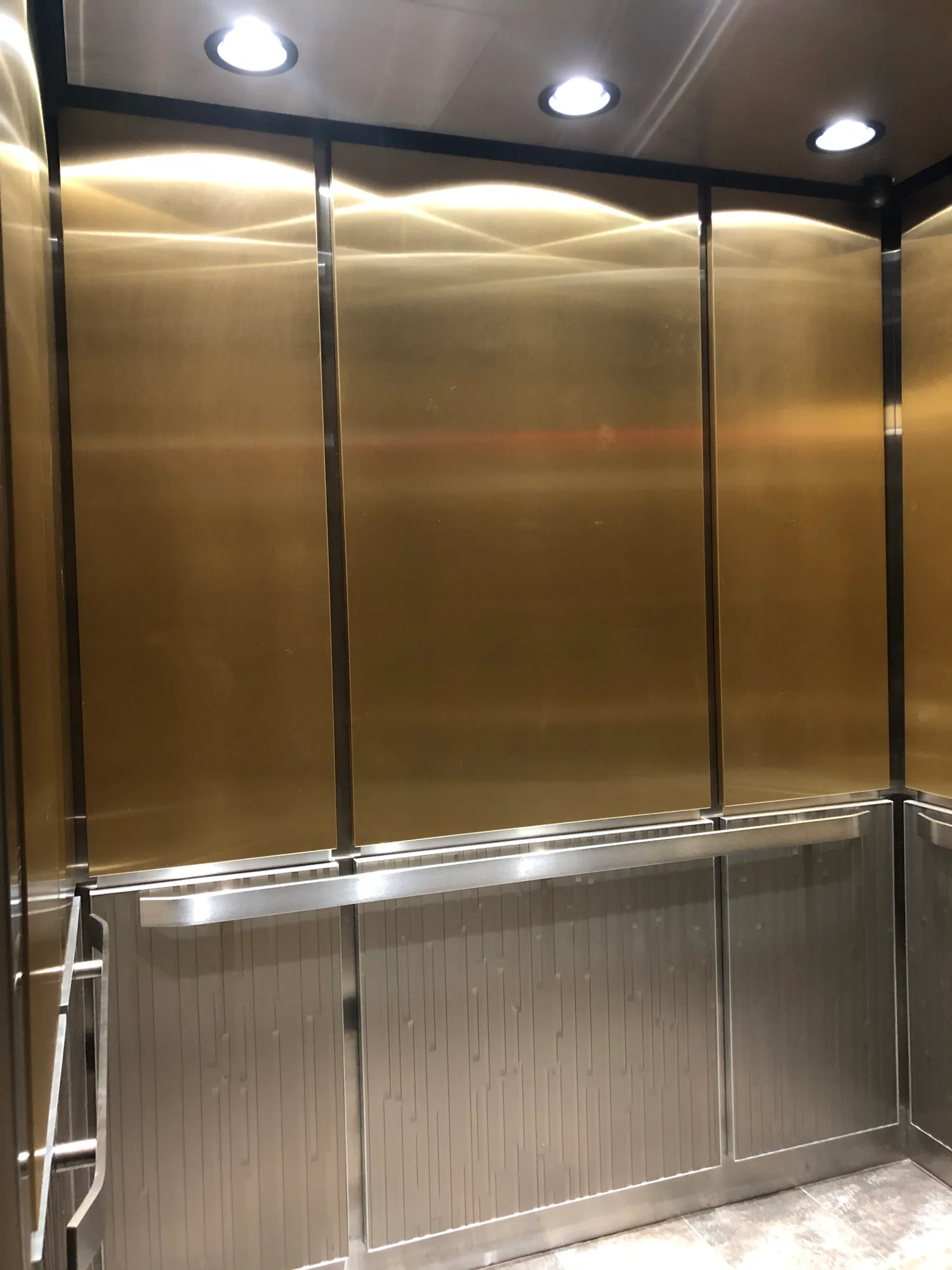 Brushed metal elevator cab with continuous stainless handrails and recessed downlights